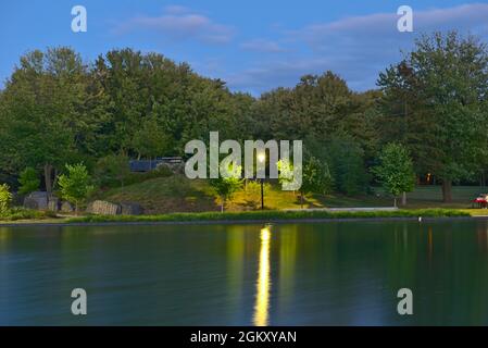 Une longue exposition du lac Beaver, Mont-Royal, Montréal, QC, Canada à l'heure bleue au crépuscule, par une journée d'été nuageuse. Les lumières et les arbres réfléchissent sur la Banque D'Images