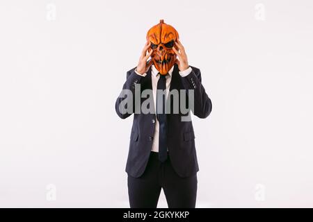 Homme habillé en costume de veste, cravate bleue et masque de citrouille Jack-o-lanterne, mains sur la tête, comme fou. Halloween et fête du carnaval. Banque D'Images