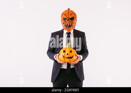 Homme vêtu d'une veste de costume, d'une cravate bleue et d'un masque de citrouille Jack-o-lanterne, tenant un crâne diabolique. Halloween et fête du carnaval. Banque D'Images