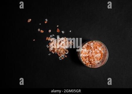 Image en hauteur d'une petite pile de pierres de sel de l'Himalaya à l'intérieur et à l'extérieur d'un contenant en verre sur fond noir Banque D'Images