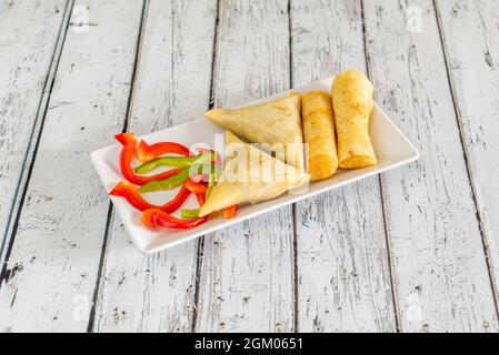 Plateau de samosas de légumes, d'en-cas indiens et de tranches de poivron rouge et vert sur des meas blancs Banque D'Images