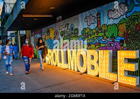 Des femmes marchent devant un panneau lumineux pour Roll Mobile, la soirée de patinage mensuelle de la ville, sur la rue Dauphin, le 10 septembre 2021, dans Mobile, Alabama. Banque D'Images