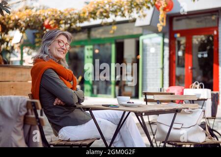 Une dame senior attentionnés aux bras croisés se trouve à table sur la terrasse du café Banque D'Images