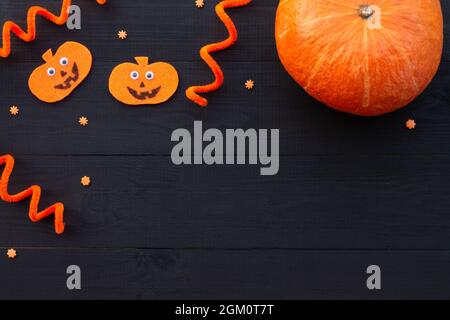 Plat d'Halloween orange et noir. Citrouilles en feutre et véritable citrouille sur fond noir en bois, espace de copie. Banque D'Images