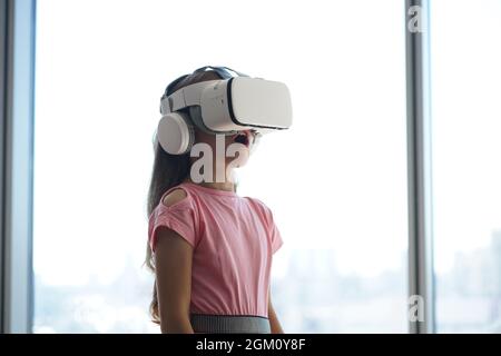 Un enfant s'amuse dans des lunettes blanches de réalité virtuelle, debout sur l'arrière-plan d'une fenêtre. Photo de haute qualité Banque D'Images