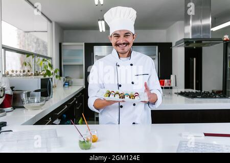 Jeune latiman chocolatier en chapeau de chef, avec bonbons mexicains au chocolat sur une assiette dans une cuisine commerciale au Mexique Amérique latine Banque D'Images