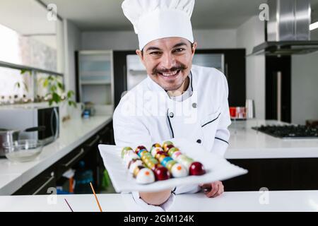 Jeune latiman chocolatier en chapeau de chef, avec bonbons mexicains au chocolat sur une assiette dans une cuisine commerciale au Mexique Amérique latine Banque D'Images