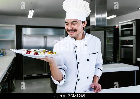 Jeune latiman chocolatier en chapeau de chef, avec bonbons mexicains au chocolat sur une assiette dans une cuisine commerciale au Mexique Amérique latine Banque D'Images