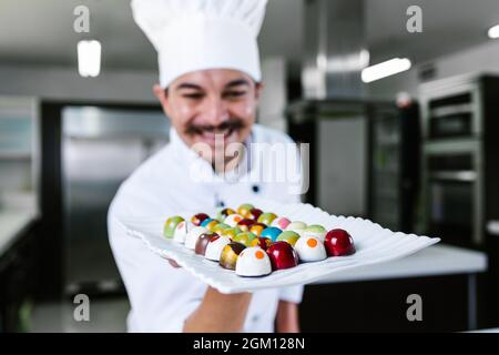 Jeune latiman chocolatier en chapeau de chef, avec bonbons mexicains au chocolat sur une assiette dans une cuisine commerciale au Mexique Amérique latine Banque D'Images