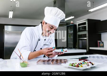 Jeune latiman chocolatier en chapeau de chef, avec bonbons mexicains au chocolat sur une assiette dans une cuisine commerciale au Mexique Amérique latine Banque D'Images