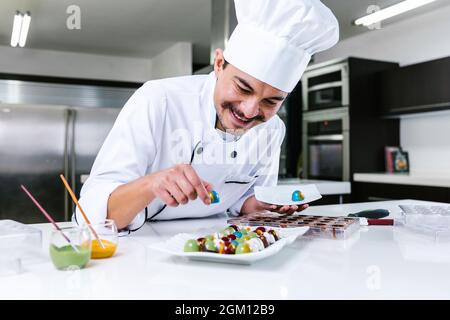 Jeune latiman chocolatier en chapeau de chef, avec bonbons mexicains au chocolat sur une assiette dans une cuisine commerciale au Mexique Amérique latine Banque D'Images