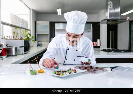 Jeune latiman chocolatier en chapeau de chef, avec bonbons mexicains au chocolat sur une assiette dans une cuisine commerciale au Mexique Amérique latine Banque D'Images