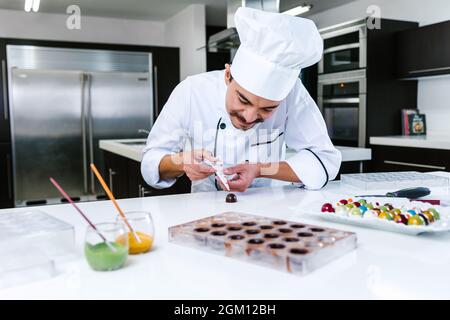 Jeune latiman chocolatier en chapeau de chef, avec bonbons mexicains au chocolat sur une assiette dans une cuisine commerciale au Mexique Amérique latine Banque D'Images