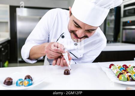 Jeune latiman chocolatier en chapeau de chef, avec bonbons mexicains au chocolat sur une assiette dans une cuisine commerciale au Mexique Amérique latine Banque D'Images