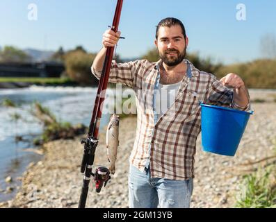 Pêcheur de poissons heureux avec un crochet et une canne à pêche dans ses mains Banque D'Images