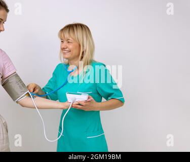 Le médecin positif en uniforme médical turquoise mesure la pression du patient à l'aide de dispositifs médicaux. Médecine et assurance. Examen préventif. Banque D'Images