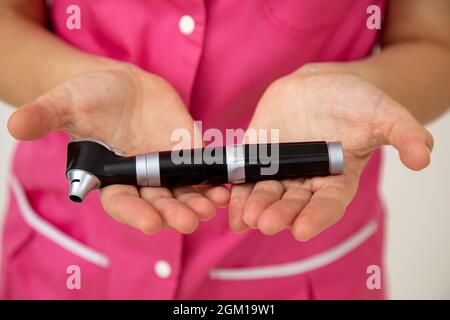 La femme médecin en vêtements médicaux roses tient l'otoscope dans ses mains . Recherche médicale. Examens préventifs. Médecine et assurance. Protection de la santé Banque D'Images