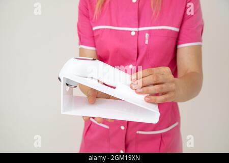 La femme cosmétologue en uniforme rose tient un dispositif laser pour le soin de la peau du visage et du corps dans ses mains. Jeunesse et beauté. Cosmétologie. Dermatologie. B Banque D'Images