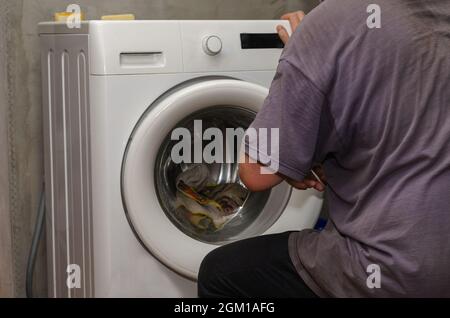 Un homme adulte à côté d'un lave-linge. Une main ferme la porte o Banque D'Images