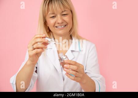 Le cosmétologue blond en uniforme médical blanc démontre qu'il travaille avec des produits de soins du visage. Acide hyaluronique. Salons de beauté. Cosmétologie moderne. La vie Banque D'Images