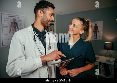 Un médecin de race masculine mixte et une infirmière caucasienne discutant tout en discutant de la recherche sur la tablette numérique Banque D'Images