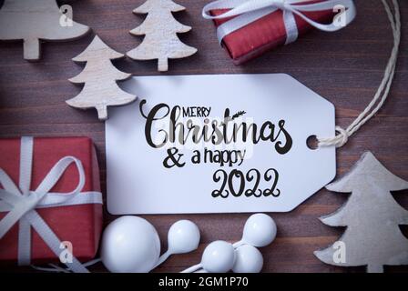 Une étiquette avec la calligraphie anglaise Joyeux Noël et heureux 2022. Décoration de Noël comme des cadeaux et des arbres. Arrière-plan en bois Banque D'Images