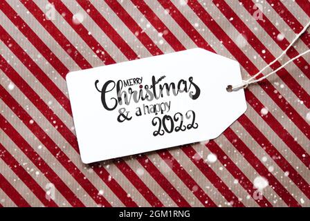 Étiquette avec la calligraphie anglaise Joyeux Noël et Un heureux 2022. Papier d'emballage rouge comme arrière-plan avec flocons de neige Banque D'Images