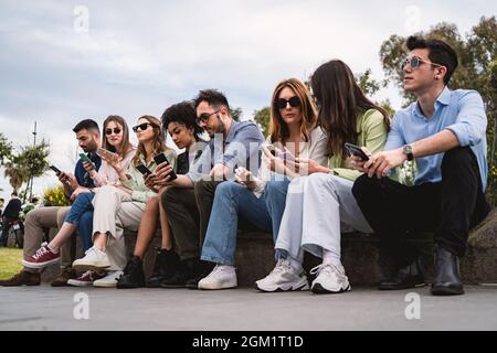 Des jeunes de génération z assis sur un banc et utilisant un smartphone. Concept de jeunes dépendants de la technologie et du réseau social. Banque D'Images