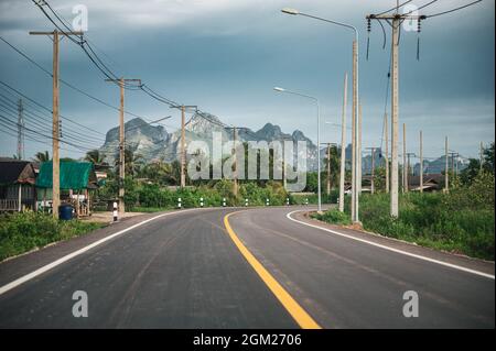 Route asphaltée courbée avec chaîne de montagnes et poteau utilitaire et lampadaire en campagne à Sam Roi Yot, Prachuap Khiri Khan Banque D'Images