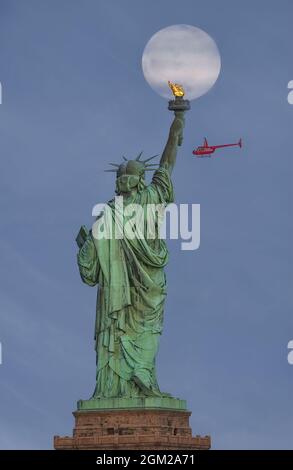 Statue de la Lune des fleurs - la lune des fleurs s'élève au-dessus de la Statue de la liberté. La grande pleine lune s'aligne parfaitement avec les statues Banque D'Images