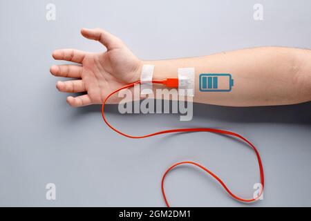 Câble de chargement USB branché sur un bras mâle avec symbole de chargement de la batterie. Fatigue, recharge, vitalité, endurance, surtâches, endurance, fatigue ou vie Banque D'Images