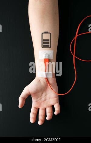 Câble de chargement USB branché sur un bras mâle avec symbole de chargement de la batterie. Fatigue, recharge, surcharge, épuisement, fatigue ou concept d'énergie de la vie. Banque D'Images