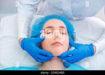 Femme visage dans les mains du médecin chirurgien plastique. Jeune femme patiente se trouve sur la table chirurgicale avant les procédures de traitement de beauté Plastic chirurgie rendez-vous Banque D'Images