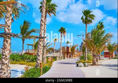 Profitez d'une promenade le long de la promenade piétonne sinueuse en bois de la plage publique de la Mer, bordée de palmiers et de plantes luxuriantes, Dubaï, Émirats Arabes Unis Banque D'Images