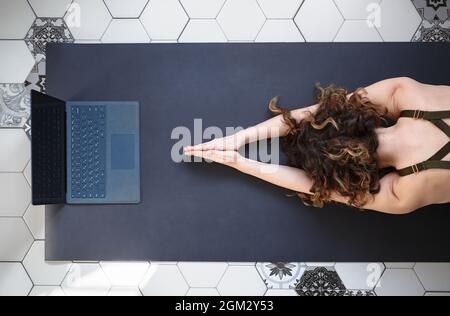 Jeune femme faisant des exercices de yoga en ligne. Yogini athlète s'étirant à la maison sur le tapis devant l'ordinateur portable, tiré directement d'en haut. Banque D'Images