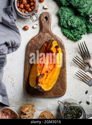 Citrouille rôtie sur une planche à découper en bois entourée de produits de saison d'automne. Kale, pain, noix et graines. Vue de dessus, arrière-plan du cadre alimentaire. Banque D'Images