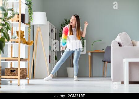 Vue sur toute la longueur du corps de belle gaie folle joyeuse fille dansant avec la brosse duveteuse avoir des vacances amusantes à la maison à l'intérieur Banque D'Images