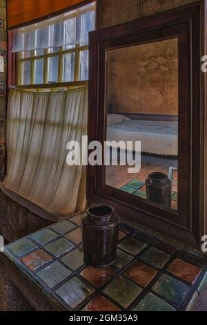 Chambre à coucher Reflections - Un lit simple se reflète dans un miroir dans le château éclectique. Le miroir repose sur une table recouverte de carreaux colorés et de nex Banque D'Images