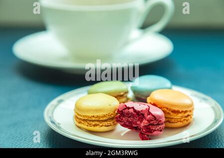 Assortiment de macarons colorés sur l'assiette avec une tasse de thé en arrière-plan. Banque D'Images