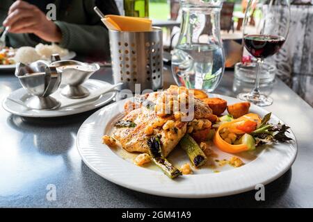 Dîner dans le restaurant extérieur. Assiette avec steak de poulet, asperges et crevettes, pommes de terre et légumes frits, bol avec mayonnaise, verre de vin et wate Banque D'Images