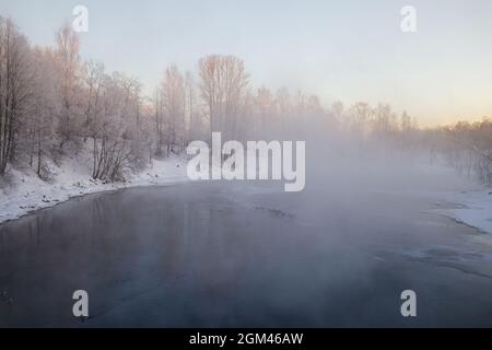Fond hiver naturel gelé. La vapeur s'élève au-dessus de l'eau d'une rivière qui ne gèle pas en forte gelée. Paysage matinal en début d'hiver Banque D'Images