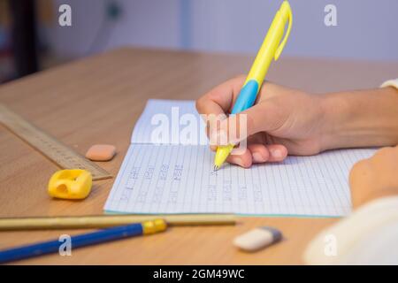 La main de l'élève écrit avec un stylo à bille dans un ordinateur portable gros plan. Un écolier effectue une tâche sur le lieu de travail. Le concept de l'éducation, de l'enseignement des connaissances, des compétences et des capacités des enfants. Banque D'Images