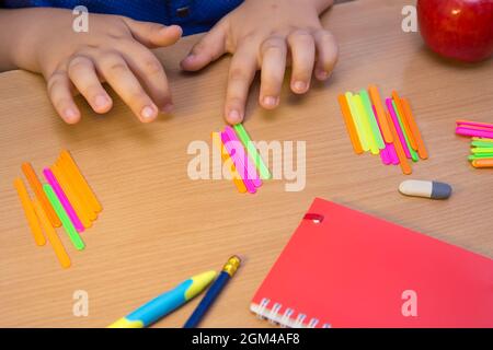 Les mains de l'étudiant sont comptées comme des bâtons multicolores en gros plan. Un écolier effectue une tâche sur le lieu de travail. Le concept de l'éducation, de l'enseignement des connaissances, des compétences et des capacités des enfants. Banque D'Images