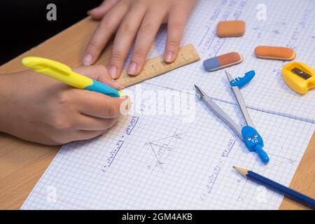 La main de l'élève en gros plan résout un problème de géométrie dans un bloc-notes. Un écolier effectue une tâche sur le lieu de travail. Le concept de l'éducation, de l'enseignement des connaissances, des compétences et des capacités des enfants. Banque D'Images