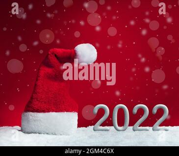 Chapeau de père Noël sur neige sur fond rouge, décoration de Noël. Concept de vacances. 2022. Banque D'Images