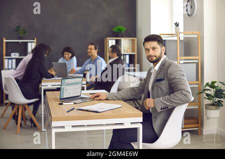 Beau homme millénaire élégant assis au bureau dans le bureau du centre d'affaires moderne. Banque D'Images