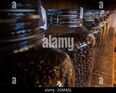 Emballage du pot en verre aux grains de café noirs sur un support en bois, à l'arrière-plan du café. Café fraîchement torréfié sur une bouteille maison. Banque D'Images