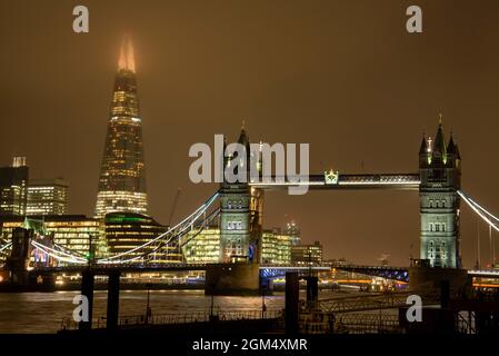 Tower Bridge et le Shard de Londres lors d'une soirée brumeuse avec des lumières lumineuses. Banque D'Images