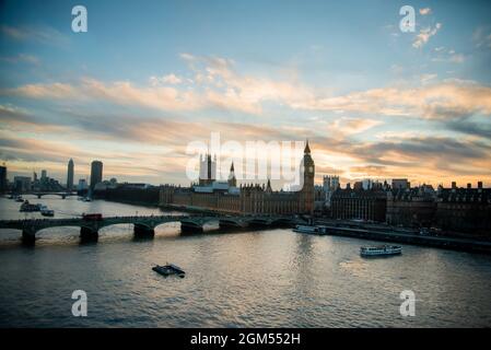 Vue sur la ville de Londres au coucher du soleil avec des monuments célèbres, Big Ben, le Parlement et des navires sur la Tamise avec un magnifique ciel bleu et jaune. Banque D'Images