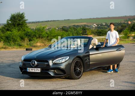 Dnepropetrovsk, Ukraine - 08.24.2021: Jeune homme près de Mercedes Benz voiture luxe transport style de vie. Mercedes Benz SL550 CABRIOLET sur la route. Banque D'Images